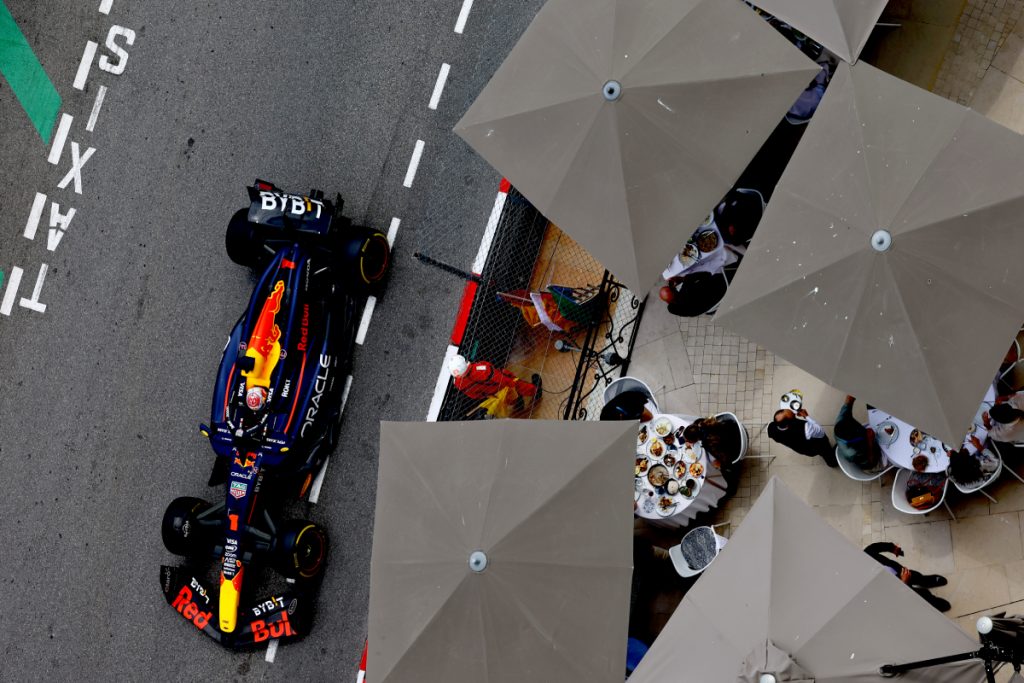 Max Verstappen en acción en Mónaco mientras otros comen en una terraza